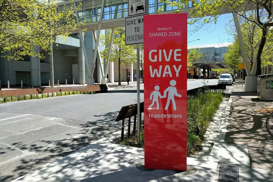 Red sign with "Give Way" and pedestrian icons on 'shared street' with 15kph speed limit in Canberra, Australia.